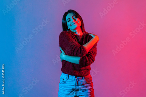Obraz na plátně I love myself! Neon light portrait of selfish narcissistic woman embracing herself and smiling with pleasure expression, positive self-esteem and complacency concept