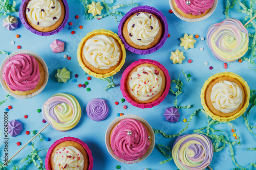 Multi-colored cupcakes with cream and meringue on a blue background. Birthday baking. Holiday pastries. Sweet dessert. Confectionery. Cupcake with a birthday candle. Treats for the party.