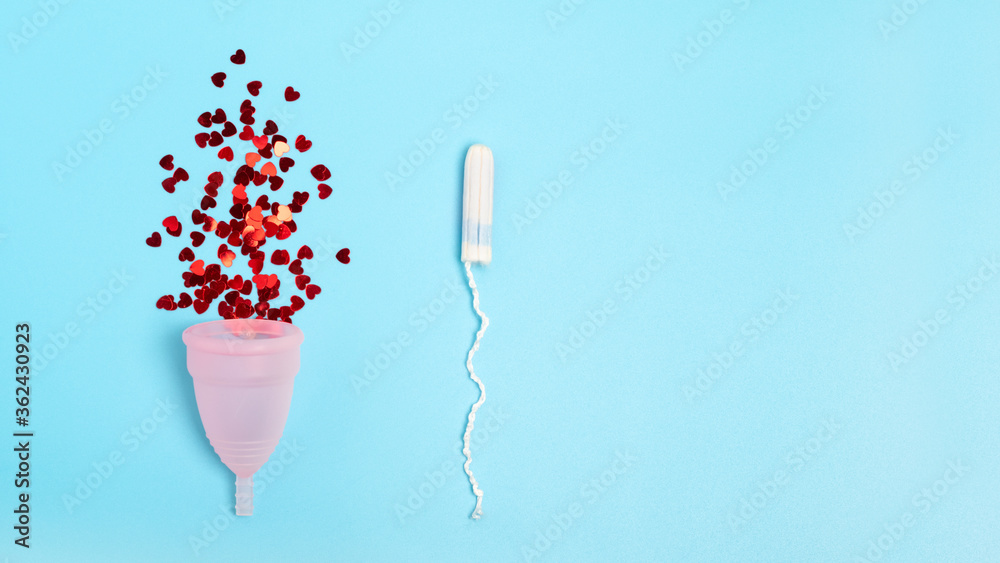 Ecological reusable pink menstrual cup or tampon with confit hearts on a blue background. Flat lay with copy space. Environmental awareness, eco friendly, zero waste, choise, vs concept. Ecological reusable pink menstrual cup or tampon with confit hearts on a blue background. Flat lay with copy space. Environmental awareness, eco friendly, zero waste, choise, vs concept.