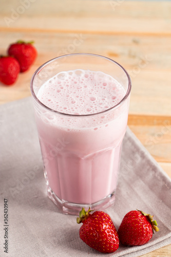 Milkshake with strawberries. Cold summer drink with berries on wooden background.