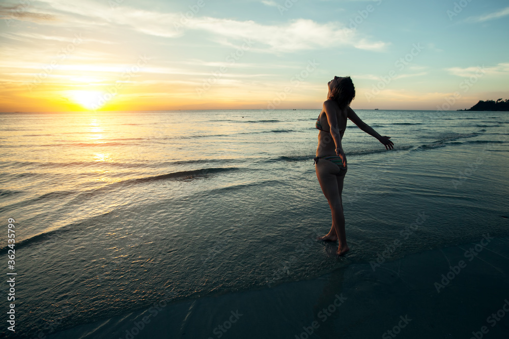 A young woman sees off the sun on a tropical beach.