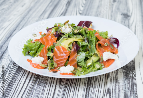 salad with vegetables and red fish on a white plate