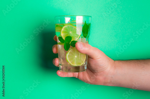 Homem branco segurando um copo de limonada fresca com pedaços de limão e manjericão sobre o fundo verde photo