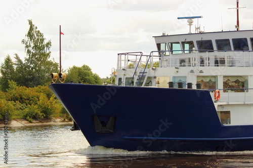 Bow of blue white Russian passenger cruise boat closeup side view on green river shore background on summer day - ship travel vacation  water tourism