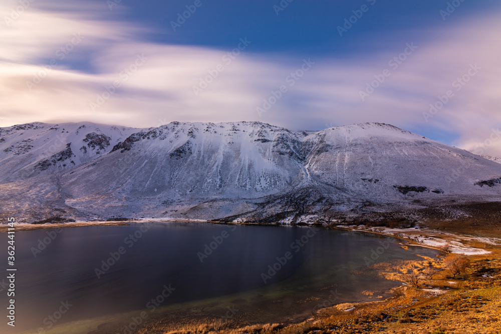 Fototapeta Long exposure shot of a mountain lake against snow-capped mountains during the sunset in winter, Esquel, Patagonia, Argentina