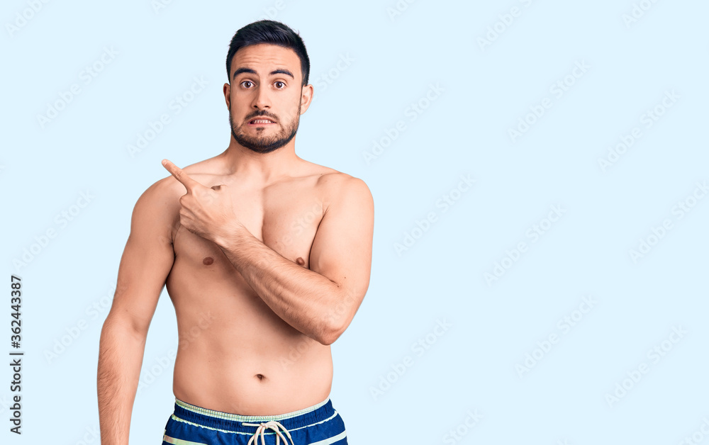 Young handsome man wearing swimwear pointing aside worried and nervous with forefinger, concerned and surprised expression