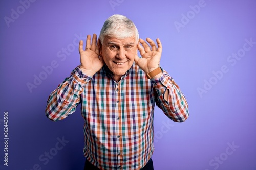 Senior handsome hoary man wearing casual colorful shirt over isolated purple background Trying to hear both hands on ear gesture, curious for gossip. Hearing problem, deaf