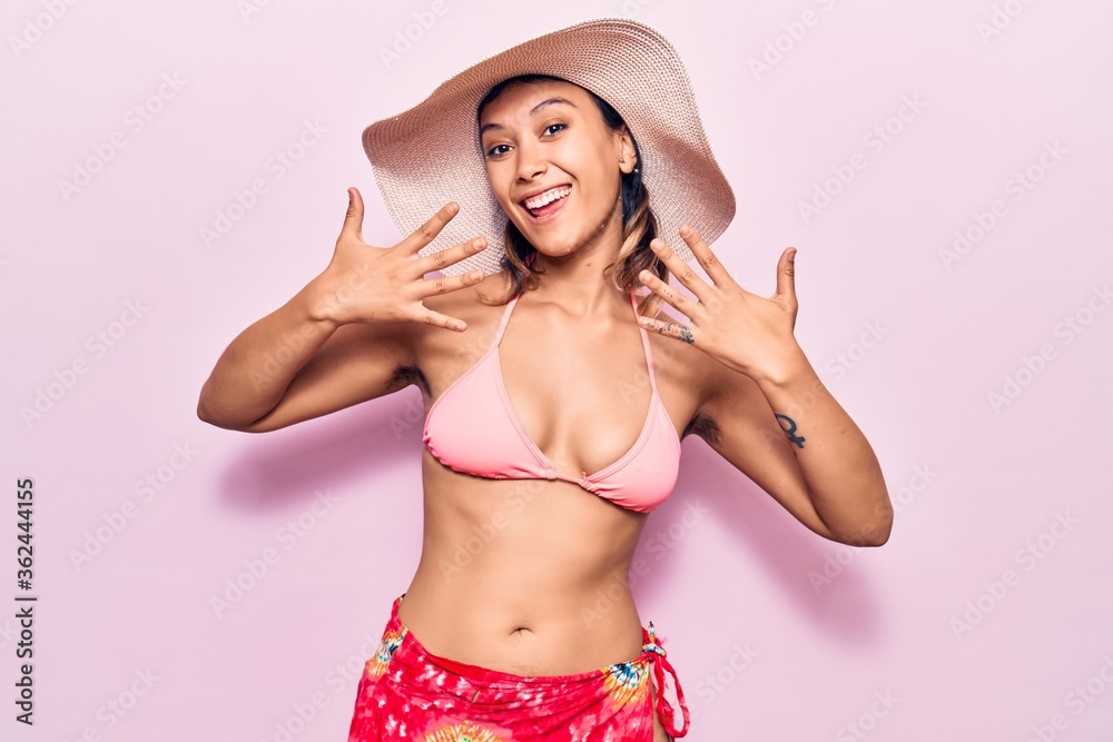 Naklejka premium Young woman wearing bikini and hat showing and pointing up with fingers number ten while smiling confident and happy.