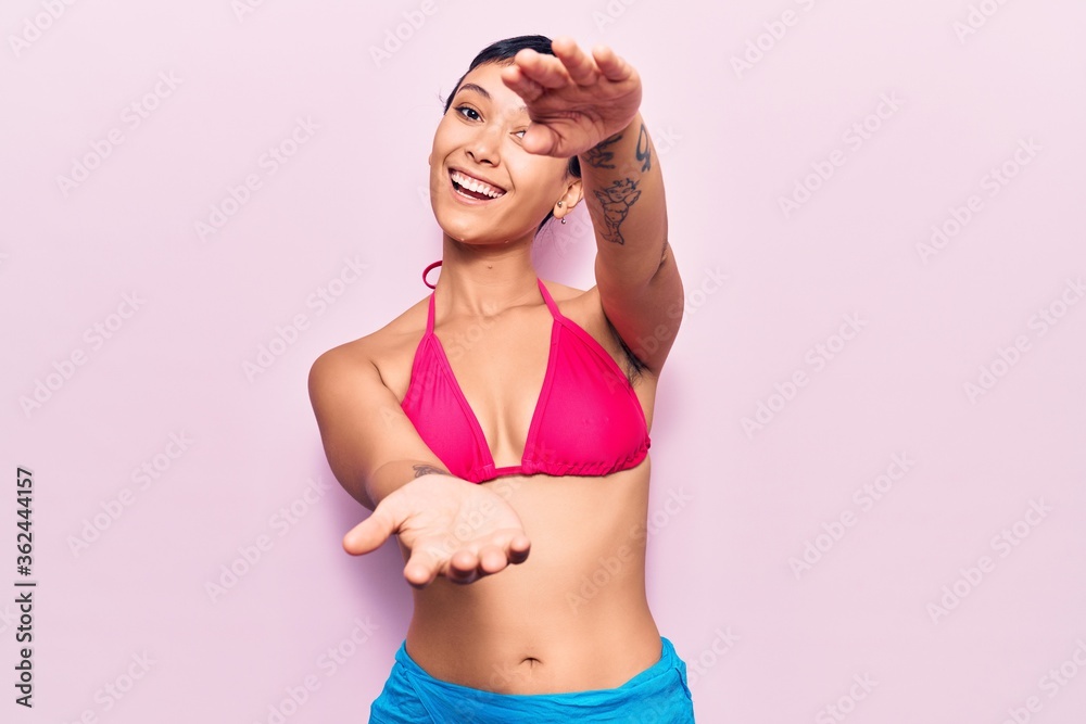 Obraz premium Young woman wearing bikini looking at the camera smiling with open arms for hug. cheerful expression embracing happiness.
