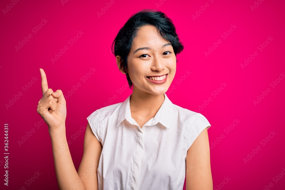 Young beautiful asian girl wearing casual summer shirt standing over isolated pink background with a big smile on face, pointing with hand and finger to the side looking at the camera. Young beautiful asian girl wearing casual summer shirt standing over isolated pink background with a big smile on face, pointing with hand and finger to the side looking at the camera.