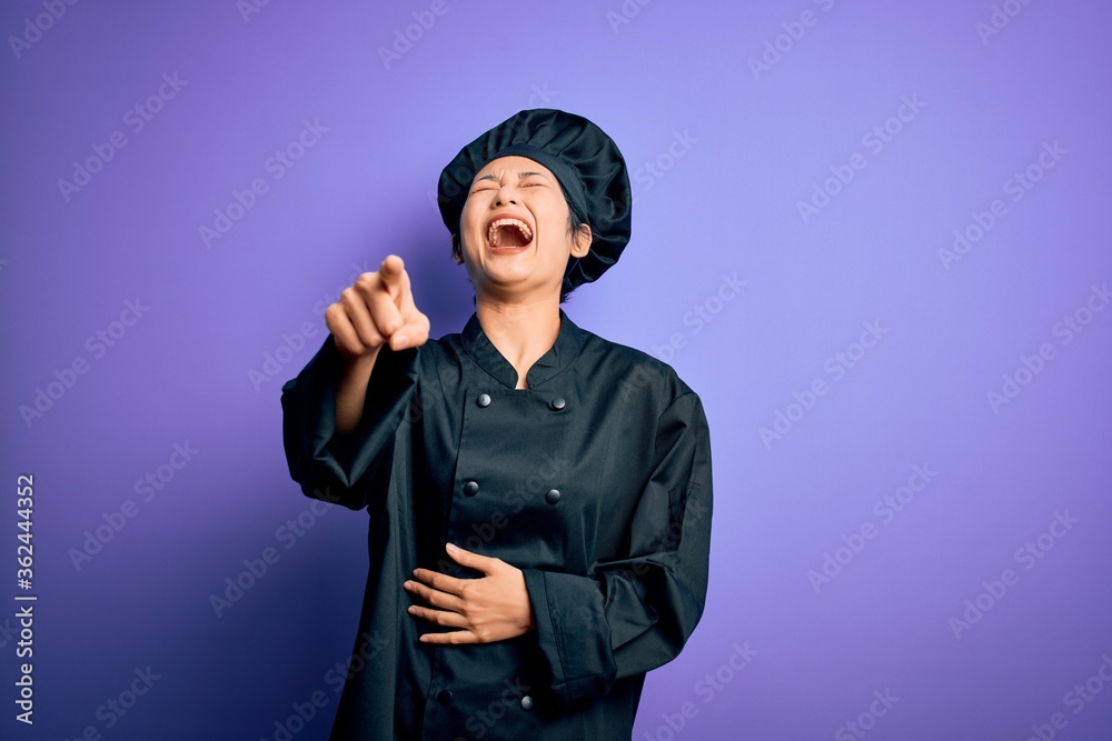 Young beautiful chinese chef woman wearing cooker uniform and hat over purple background laughing at you, pointing finger to the camera with hand over body, shame expression Young beautiful chinese chef woman wearing cooker uniform and hat over purple background laughing at you, pointing finger to the camera with hand over body, shame expression