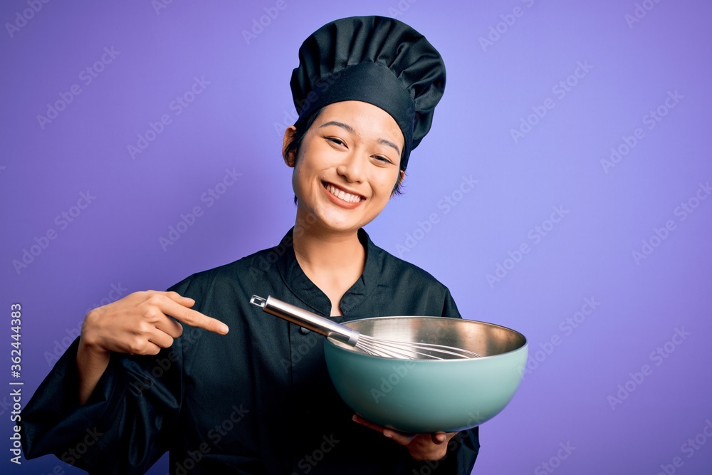 Young beautiful chinese chef woman wearing cooker uniform and hat using bowl and whisk with surprise face pointing finger to himself Young beautiful chinese chef woman wearing cooker uniform and hat using bowl and whisk with surprise face pointing finger to himself