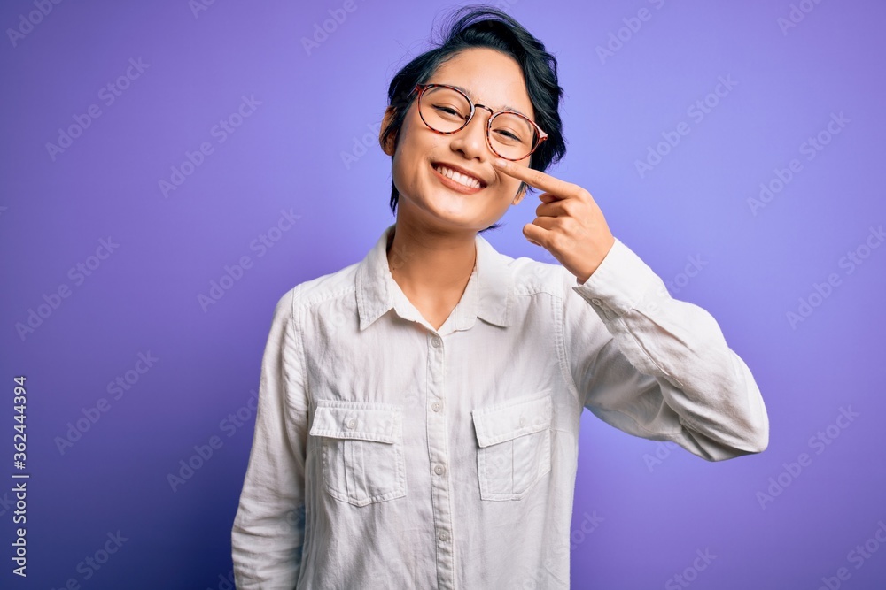 Young beautiful asian girl wearing casual shirt and glasses standing over purple background Pointing with hand finger to face and nose, smiling cheerful. Beauty concept Young beautiful asian girl wearing casual shirt and glasses standing over purple background Pointing with hand finger to face and nose, smiling cheerful. Beauty concept