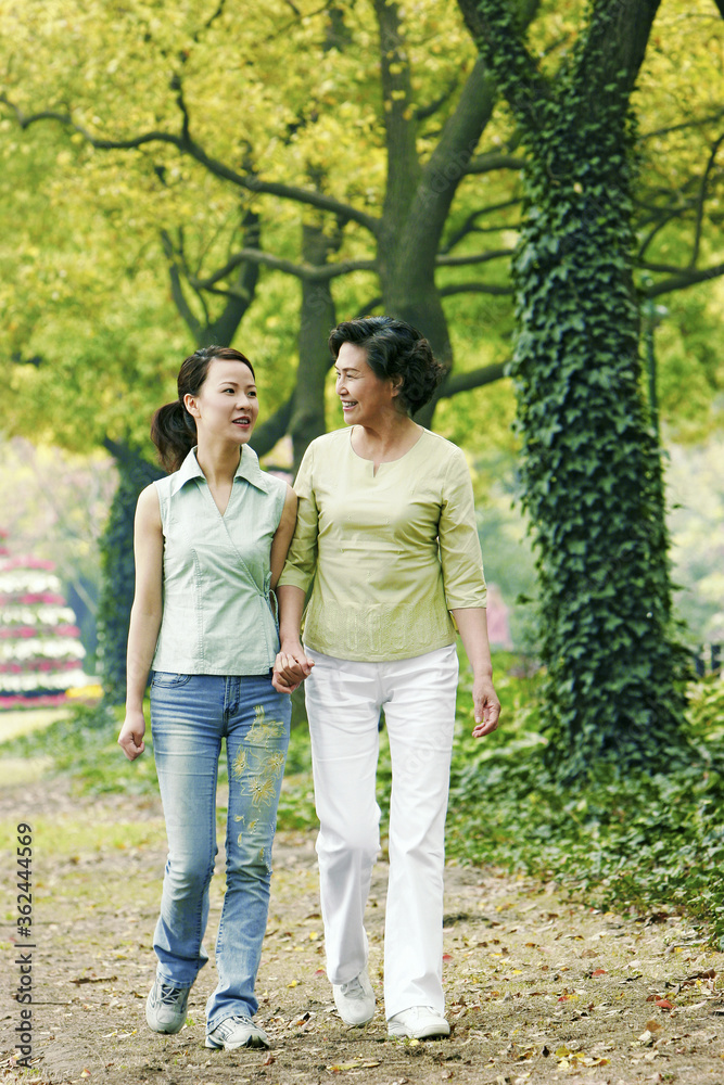 A mother and daughter holding hands walking in the park