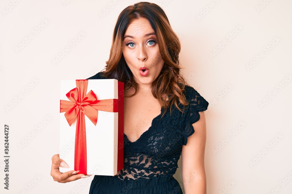 Young beautiful caucasian woman holding gift scared and amazed with open mouth for surprise, disbelief face Young beautiful caucasian woman holding gift scared and amazed with open mouth for surprise, disbelief face