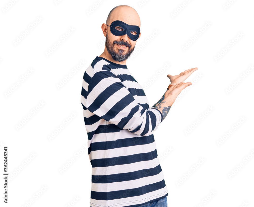 Naklejka premium Young handsome man wearing burglar mask inviting to enter smiling natural with open hand