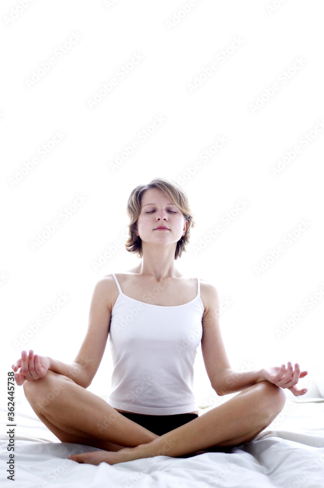 A woman in white camisole meditating on the bed A woman in white camisole meditating on the bed