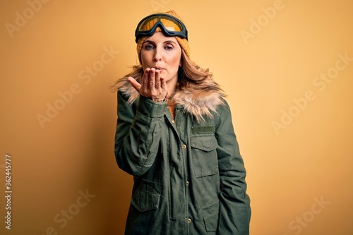 Middle age beautiful blonde skier woman wearing snow sportwear and ski goggles looking at the camera blowing a kiss with hand on air being lovely and sexy. Love expression. © Krakenimages.com