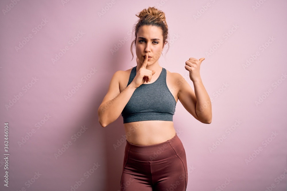 Young beautiful blonde sportswoman doing sport wearing sportswear over pink background asking to be quiet with finger on lips pointing with hand to the side. Silence and secret concept.