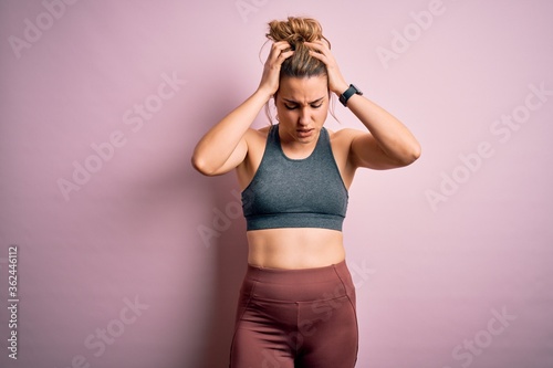 Fotografie Young beautiful blonde sportswoman doing sport wearing sportswear over pink background suffering from headache desperate and stressed because pain and migraine