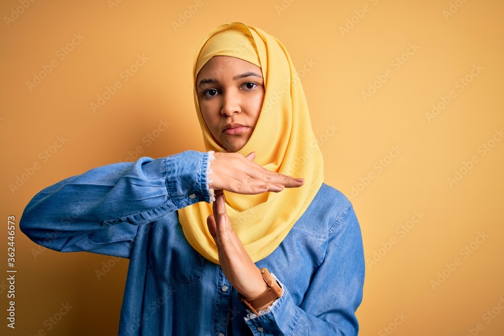 Young beautiful woman with curly hair wearing arab traditional hijab over yellow background Doing time out gesture with hands, frustrated and serious face Young beautiful woman with curly hair wearing arab traditional hijab over yellow background Doing time out gesture with hands, frustrated and serious face