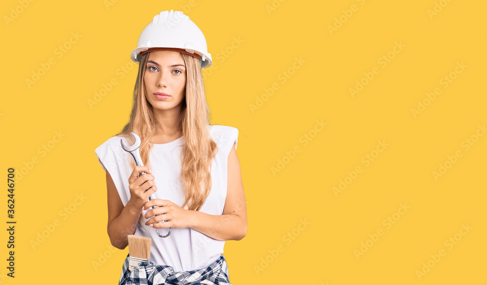 Beautiful caucasian woman with blonde hair wearing hardhat and builder clothes thinking attitude and sober expression looking self confident Beautiful caucasian woman with blonde hair wearing hardhat and builder clothes thinking attitude and sober expression looking self confident