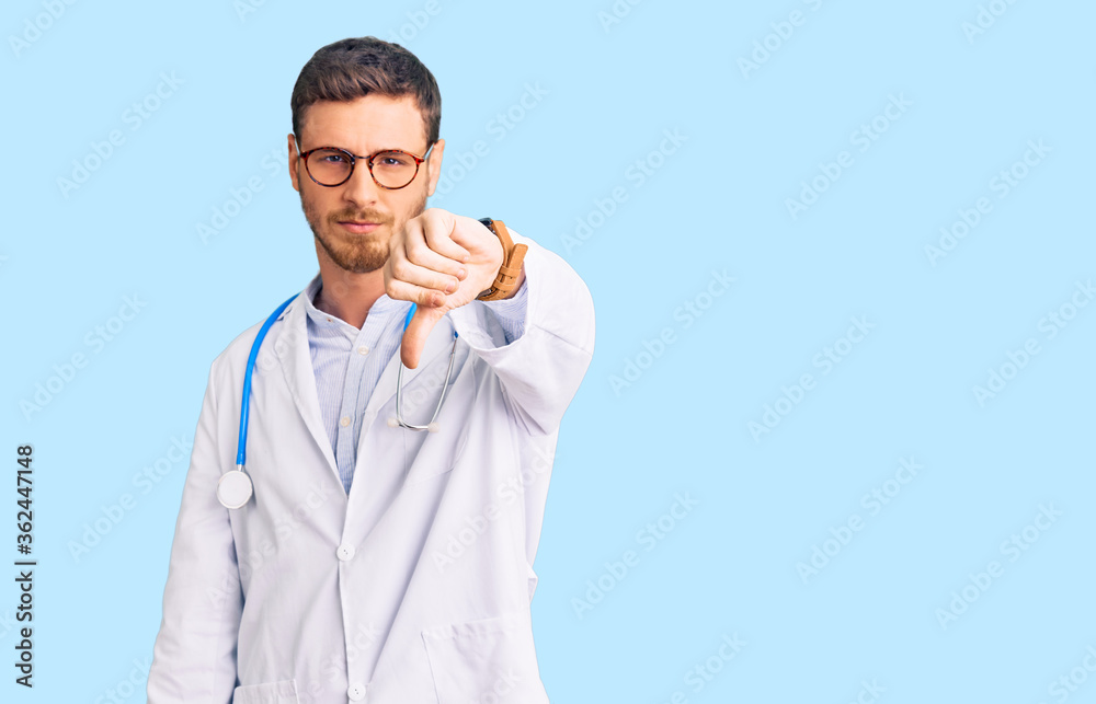 Handsome young man with bear wearing doctor uniform looking unhappy and angry showing rejection and negative with thumbs down gesture. bad expression. Handsome young man with bear wearing doctor uniform looking unhappy and angry showing rejection and negative with thumbs down gesture. bad expression.