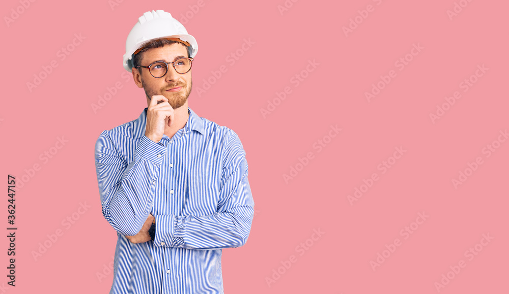 Handsome young man with bear wearing architect hardhat serious face thinking about question with hand on chin, thoughtful about confusing idea Handsome young man with bear wearing architect hardhat serious face thinking about question with hand on chin, thoughtful about confusing idea