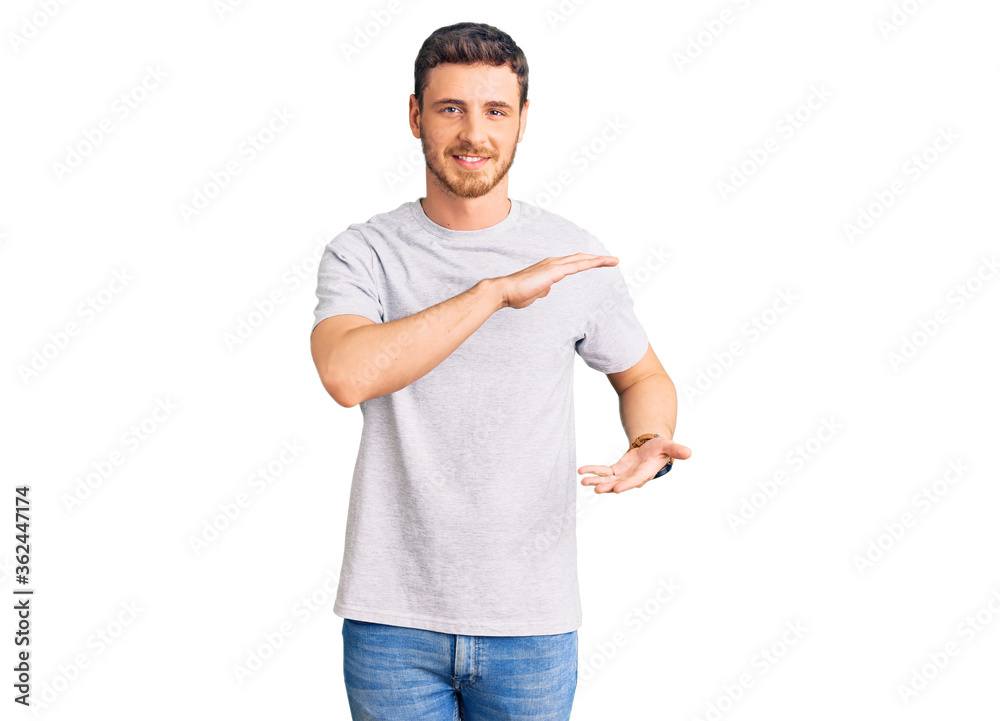 Handsome young man with bear wearing casual tshirt gesturing with hands showing big and large size sign, measure symbol. smiling looking at the camera. measuring concept.