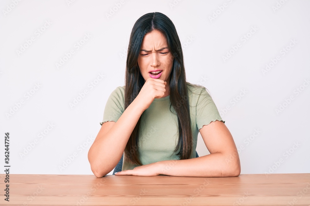 Young caucasian woman sitting at the table wearing casual clothes feeling unwell and coughing as symptom for cold or bronchitis. health care concept. Young caucasian woman sitting at the table wearing casual clothes feeling unwell and coughing as symptom for cold or bronchitis. health care concept.