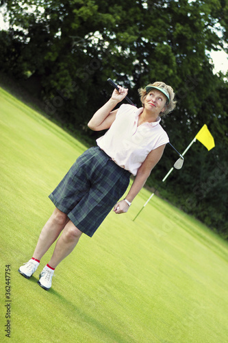 An old lady in golf attire standing in a golf course