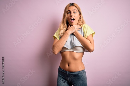 Canvastavla Young beautiful blonde sportswoman doing sport wearing sportswear over pink background shouting and suffocate because painful strangle