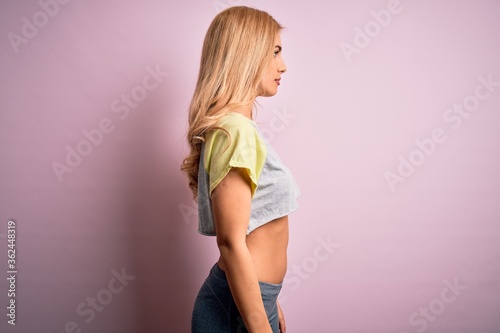 Young beautiful blonde sportswoman doing sport wearing sportswear over pink background looking to side, relax profile pose with natural face with confident smile.