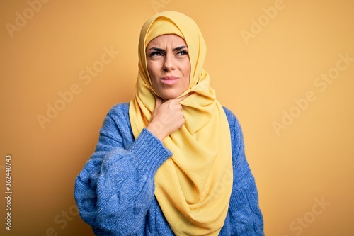 Young beautiful brunette muslim woman wearing arab hijab over isolated yellow background Touching painful neck, sore throat for flu, clod and infection © Krakenimages.com