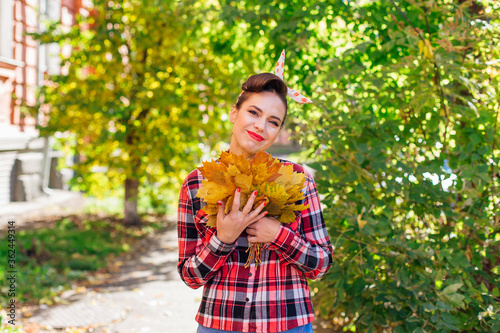 Beautiful woman with make up and hair in pin up style holding big bouquet of maple yellow leaves.