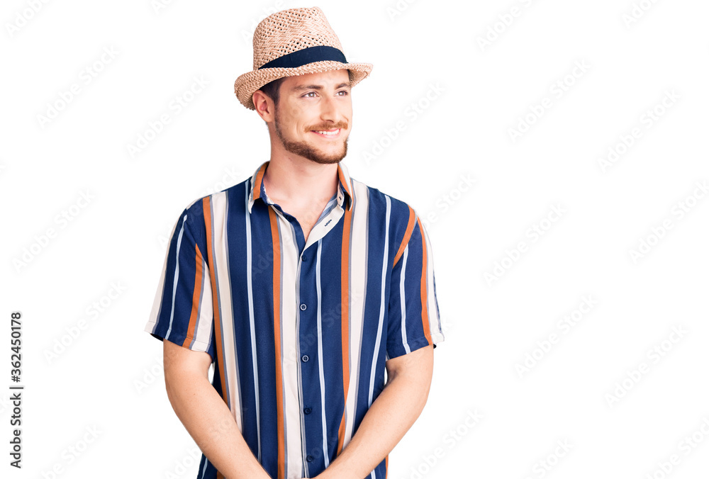 Young handsome caucasian man wearing summer hat looking away to side with smile on face, natural expression. laughing confident.
