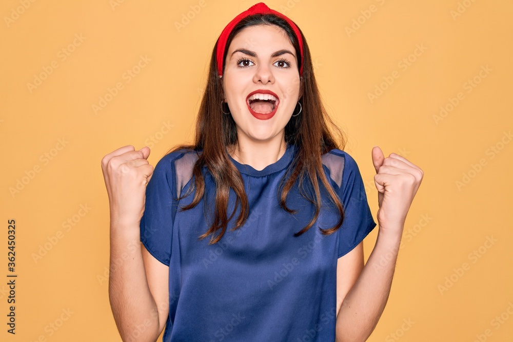 Φωτογραφία Young beautiful brunette woman wearing red lips over yellow background celebrating surprised and amazed for success with arms raised and open eyes