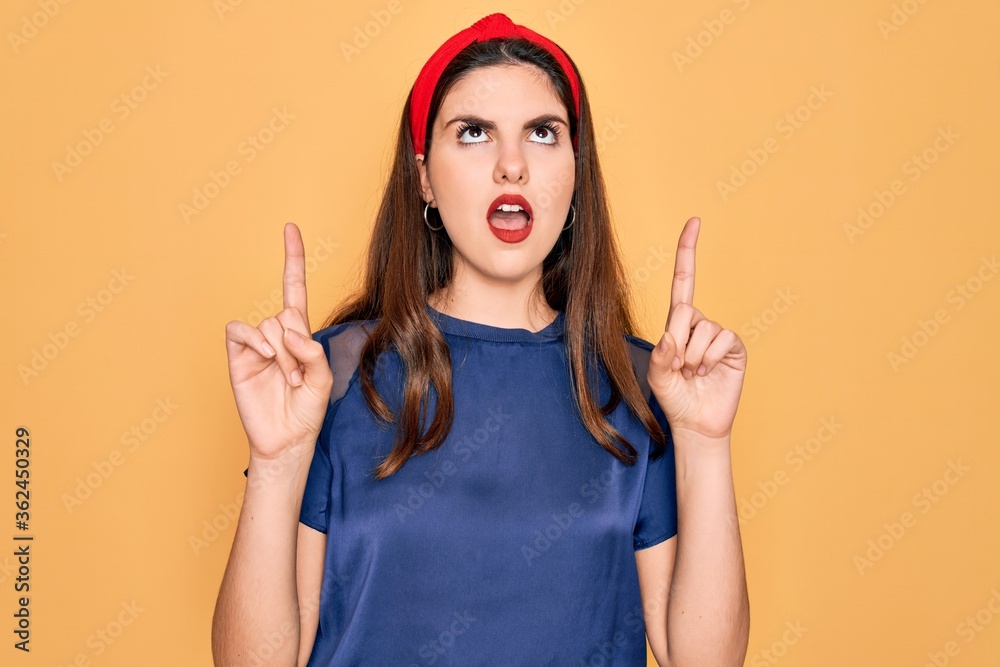 Φωτογραφία Young beautiful brunette woman wearing red lips over yellow background amazed and surprised looking up and pointing with fingers and raised arms