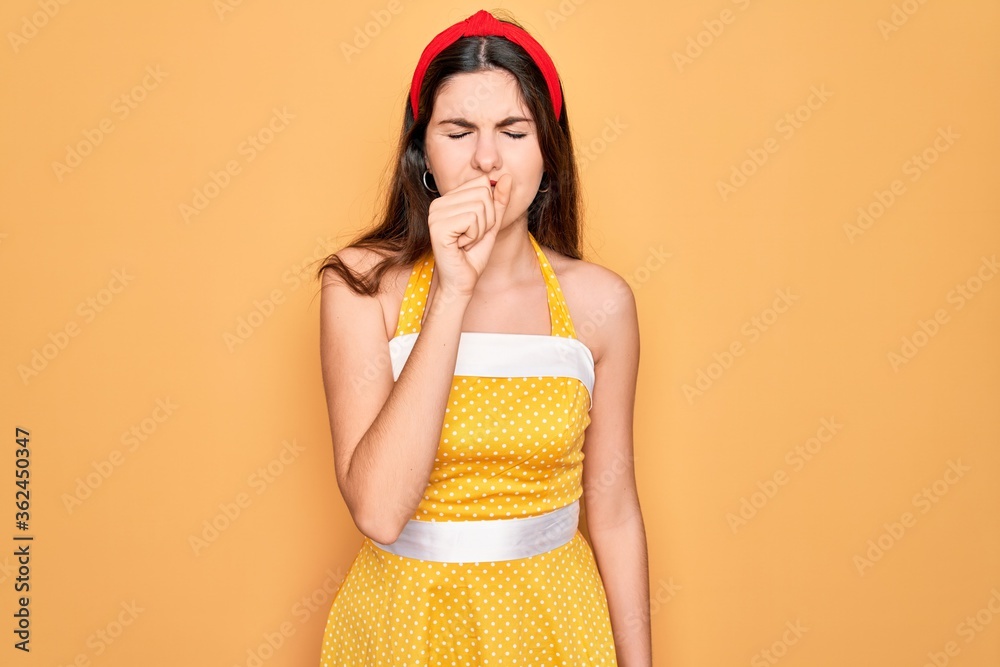 Young beautiful pin up woman wearing 50s fashion vintage dress over yellow background feeling unwell and coughing as symptom for cold or bronchitis. Health care concept. Young beautiful pin up woman wearing 50s fashion vintage dress over yellow background feeling unwell and coughing as symptom for cold or bronchitis. Health care concept.