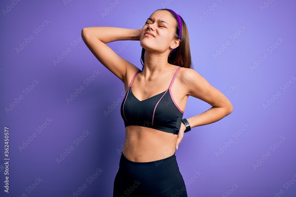 Fototapeta premium Young beautiful sporty girl doing sport wearing sportswear over isolated purple background Suffering of neck ache injury, touching neck with hand, muscular pain