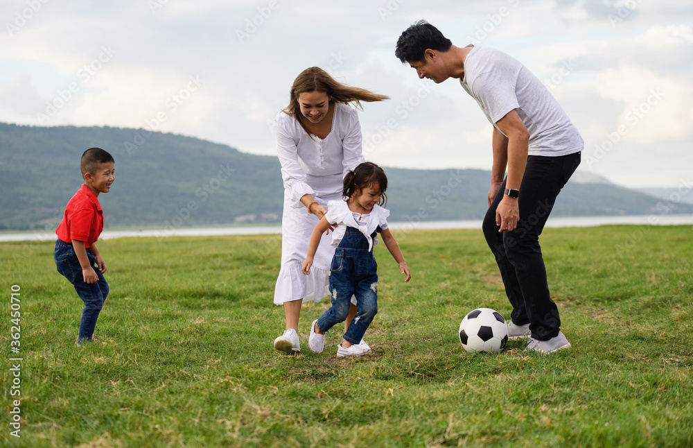 Cheerful family Asian playing football in a green lawn Cheerful family Asian playing football in a green lawn
