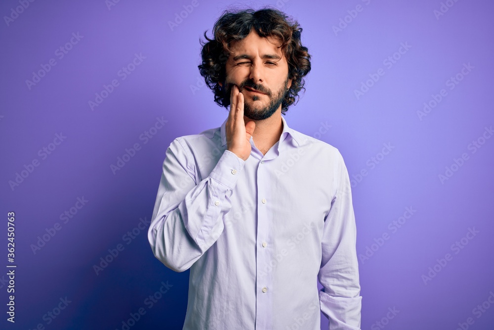 Young handsome business man with beard wearing shirt standing over purple background touching mouth with hand with painful expression because of toothache or dental illness on teeth. Dentist Young handsome business man with beard wearing shirt standing over purple background touching mouth with hand with painful expression because of toothache or dental illness on teeth. Dentist