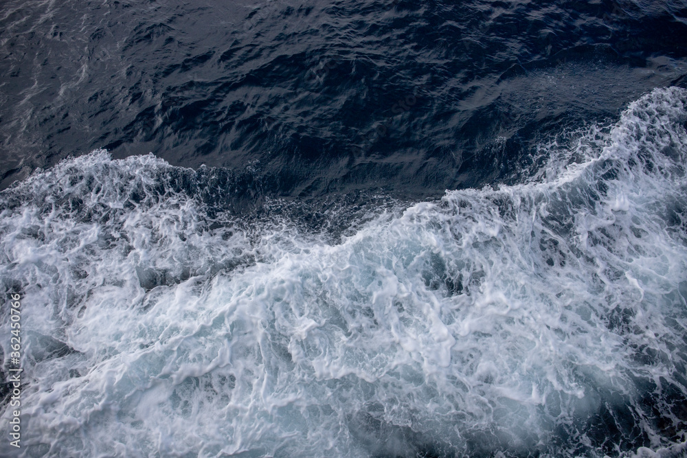 White wave splashing sea water. White foam on blue water. Maritime transportation. Ocean surface top view White wave splashing sea water. White foam on blue water. Maritime transportation. Ocean surface top view