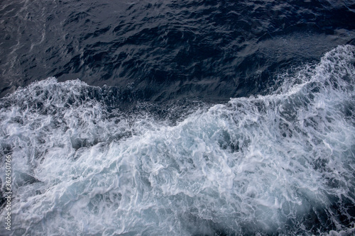 White wave splashing sea water. White foam on blue water. Maritime transportation. Ocean surface top view