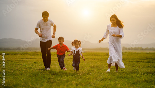 A happy Asian family run on the green lawn.
