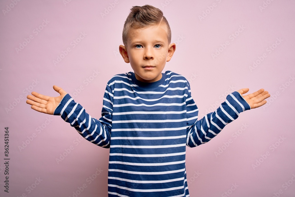 Young little caucasian kid with blue eyes wearing nautical striped shirt over pink background clueless and confused expression with arms and hands raised. Doubt concept. Young little caucasian kid with blue eyes wearing nautical striped shirt over pink background clueless and confused expression with arms and hands raised. Doubt concept.