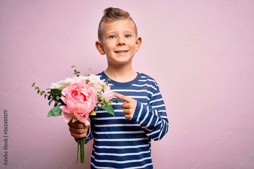 Young little caucasian kid holding romantic and cute bouquet of flowers over pink background very happy pointing with hand and finger Young little caucasian kid holding romantic and cute bouquet of flowers over pink background very happy pointing with hand and finger