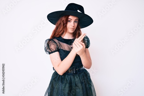 Young beautiful woman wearing witch halloween costume holding symbolic gun with hand gesture, playing killing shooting weapons, angry face © Krakenimages.com