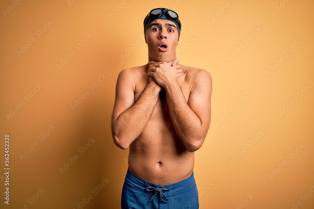 Young handsome man shirtless wearing swimsuit and swim cap over isolated yellow background shouting suffocate because painful strangle. Health problem. Asphyxiate and suicide concept.