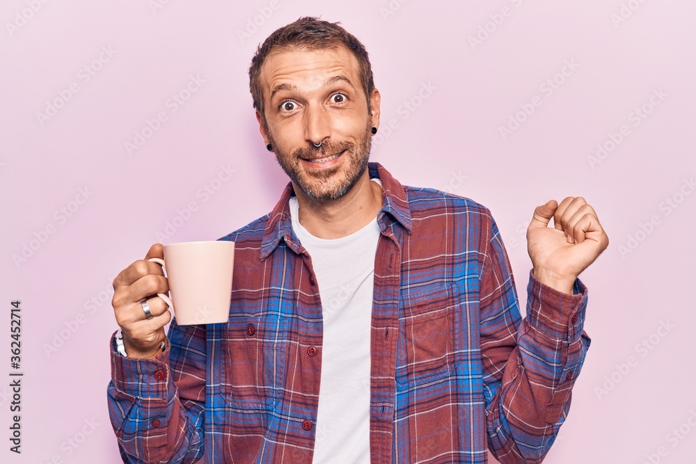Young handsome man holding coffee screaming proud, celebrating victory and success very excited with raised arm